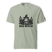 Black ink folk art illustration of a wide-eyed frog beneath an oversized pointed witch hat surrounded by cattails and marsh plants, with the words “BOG WITCH,” on a T-shirt.