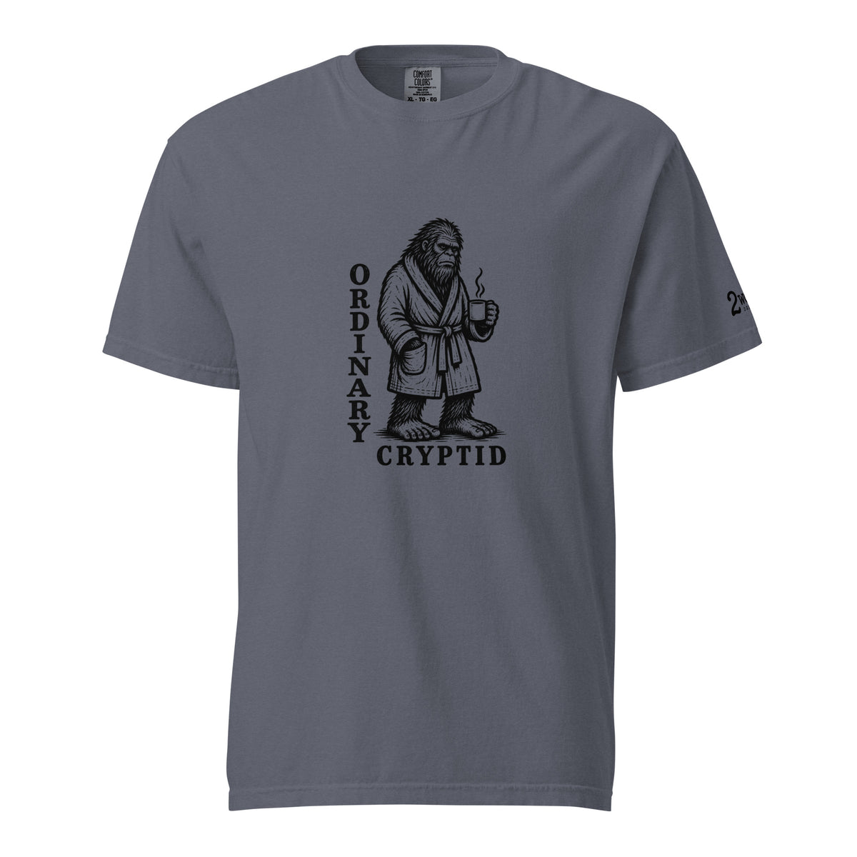 Black ink illustration of Bigfoot wearing a tied bathrobe and holding a steaming mug above the words “Ordinary Cryptid,” shown on a unisex t-shirt.