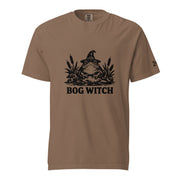 Black ink folk art illustration of a wide-eyed frog beneath an oversized pointed witch hat surrounded by cattails and marsh plants, with the words “BOG WITCH,” on a T-shirt.