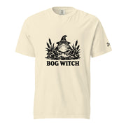 Black ink folk art illustration of a wide-eyed frog beneath an oversized pointed witch hat surrounded by cattails and marsh plants, with the words “BOG WITCH,” on a T-shirt.