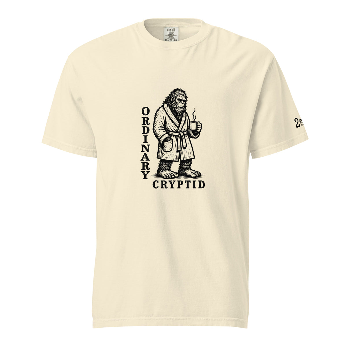 Black ink illustration of Bigfoot wearing a tied bathrobe and holding a steaming mug above the words “Ordinary Cryptid,” shown on a unisex t-shirt.