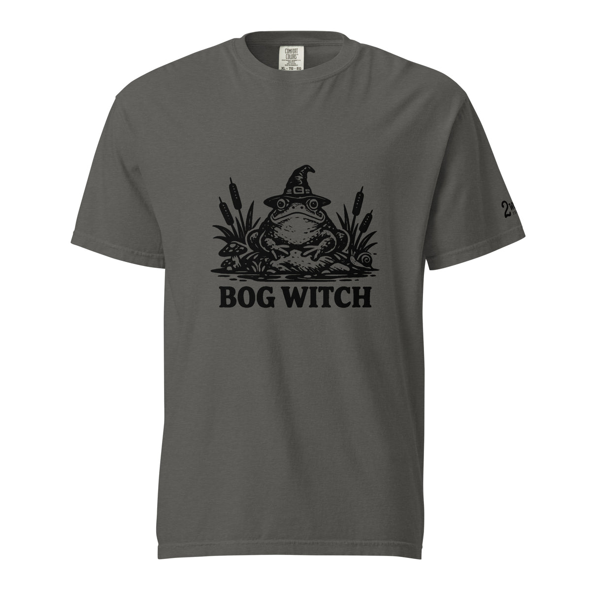 Black ink folk art illustration of a wide-eyed frog beneath an oversized pointed witch hat surrounded by cattails and marsh plants, with the words “BOG WITCH,” on a T-shirt.