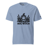 Black ink folk art illustration of a wide-eyed frog beneath an oversized pointed witch hat surrounded by cattails and marsh plants, with the words “BOG WITCH,” on a T-shirt.