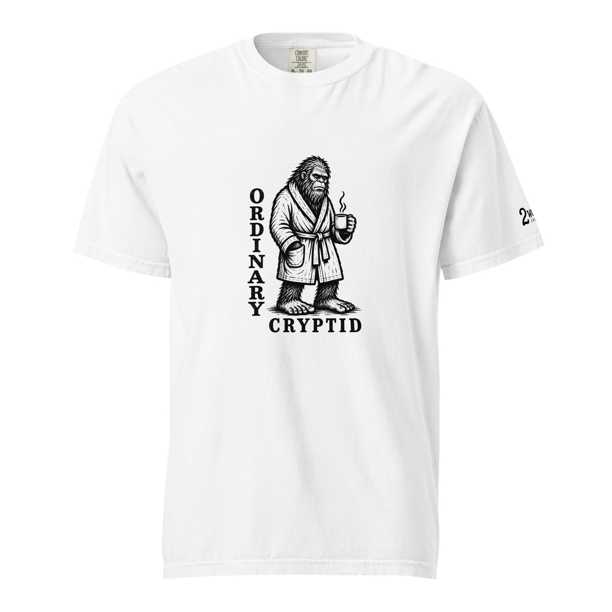 Black ink illustration of Bigfoot wearing a tied bathrobe and holding a steaming mug above the words “Ordinary Cryptid,” shown on a unisex t-shirt.