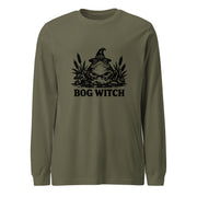 Black ink folk art illustration of a wide-eyed frog beneath an oversized pointed witch hat surrounded by cattails and marsh plants, with the words “BOG WITCH,” on a long sleeve tee.
