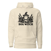 Black ink folk art illustration of a wide-eyed frog beneath an oversized pointed witch hat surrounded by cattails and marsh plants, with the words “BOG WITCH,” on a hoodie.