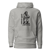 Black ink illustration of Bigfoot wearing a tied bathrobe and holding a steaming mug above the words “Ordinary Cryptid,” shown on a hoodie.