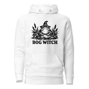 Black ink folk art illustration of a wide-eyed frog beneath an oversized pointed witch hat surrounded by cattails and marsh plants, with the words “BOG WITCH,” on a hoodie.