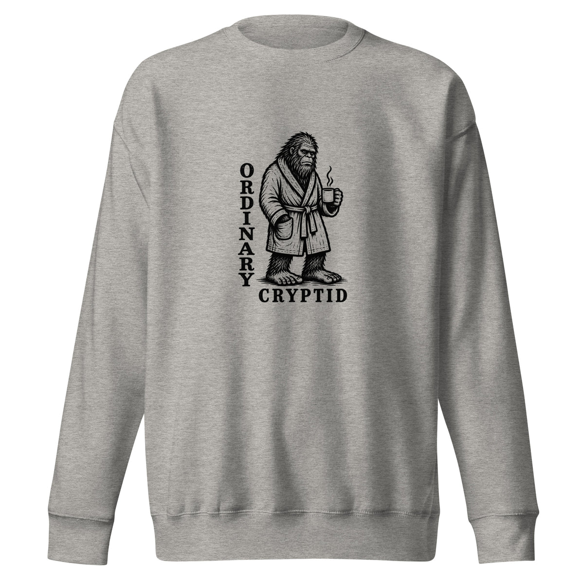 Black ink illustration of Bigfoot wearing a tied bathrobe and holding a steaming mug above the words “Ordinary Cryptid,” shown on a sweatshirt.