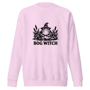 Black ink folk art illustration of a wide-eyed frog beneath an oversized pointed witch hat surrounded by cattails and marsh plants, with the words “BOG WITCH,” on a sweatshirt.