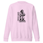 Black ink illustration of Bigfoot wearing a tied bathrobe and holding a steaming mug above the words “Ordinary Cryptid,” shown on a sweatshirt.